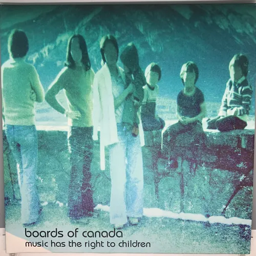 A grainy, faded vintage photograph of a family group standing at a scenic overlook, their faces blurred out, washed in cool teal and green tones with a rocky overhang framing the top.