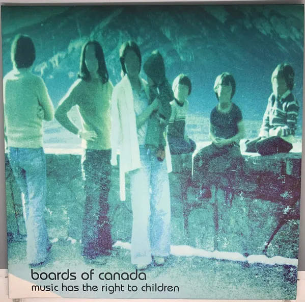 A grainy, faded vintage photograph of a family group standing at a scenic overlook, their faces blurred out, washed in cool teal and green tones with a rocky overhang framing the top.