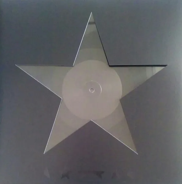 A large five-pointed star cut out of a translucent, faintly iridescent vinyl record — its circular label and center hole visible at the middle — set against a flat grey background.
