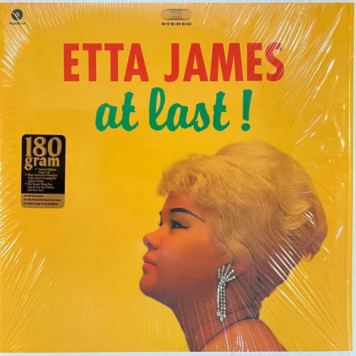 A woman shown in profile with a blonde bouffant hairstyle and a long rhinestone drop earring appears at the lower right of a bright yellow background, with red and green lettering across the top and a gold sticker at the left, all beneath a shrink-wrap sheen.