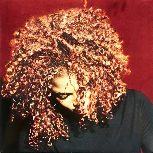 A woman with voluminous curly copper-toned hair tilts her head downward with eyes closed, her face partly veiled by ringlets, set against a deep crimson background and wearing a dark top.