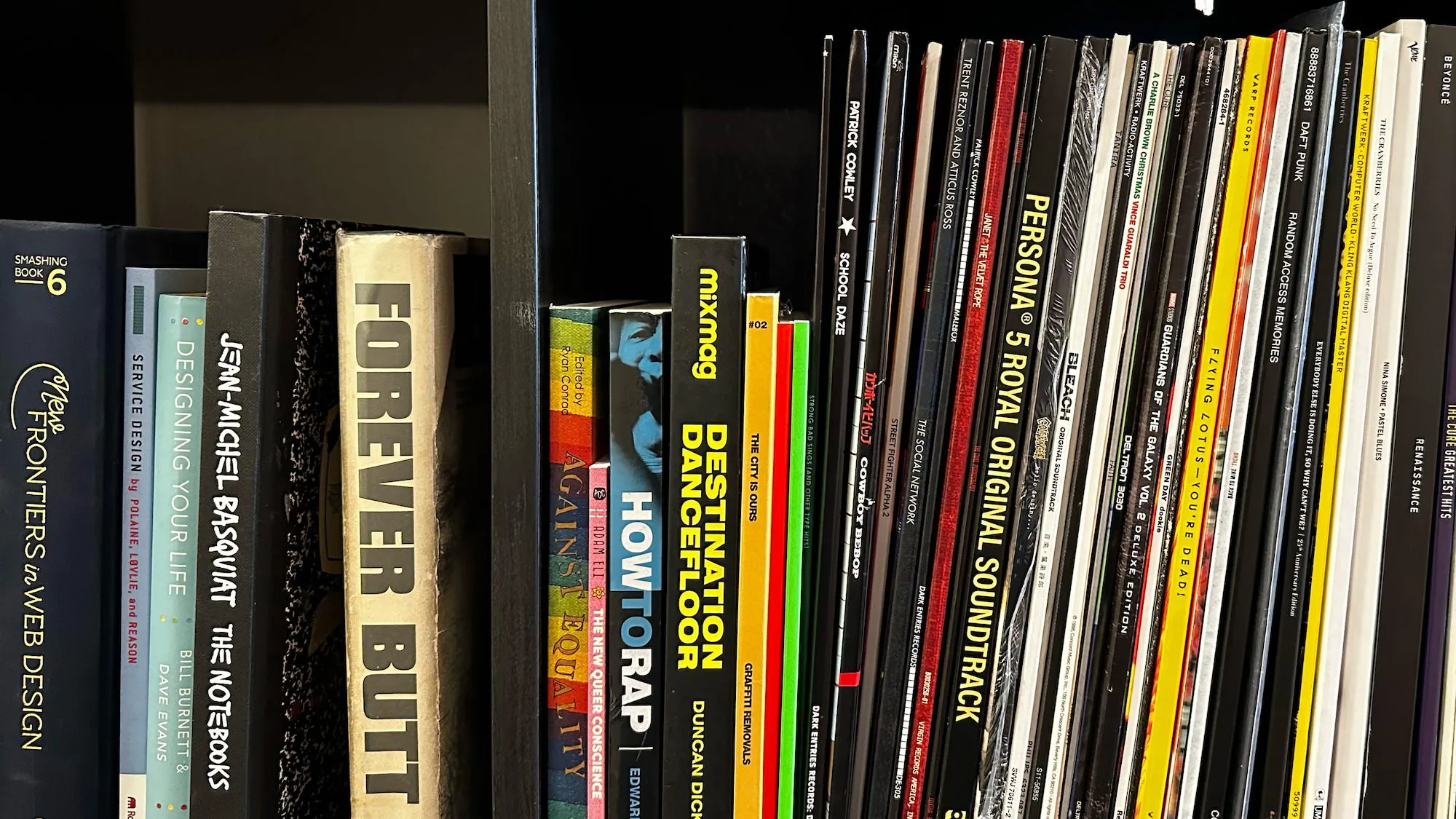 A bookshelf containing media of various different types, books, art, comics, and vinyl records, all arranged in square cubes.