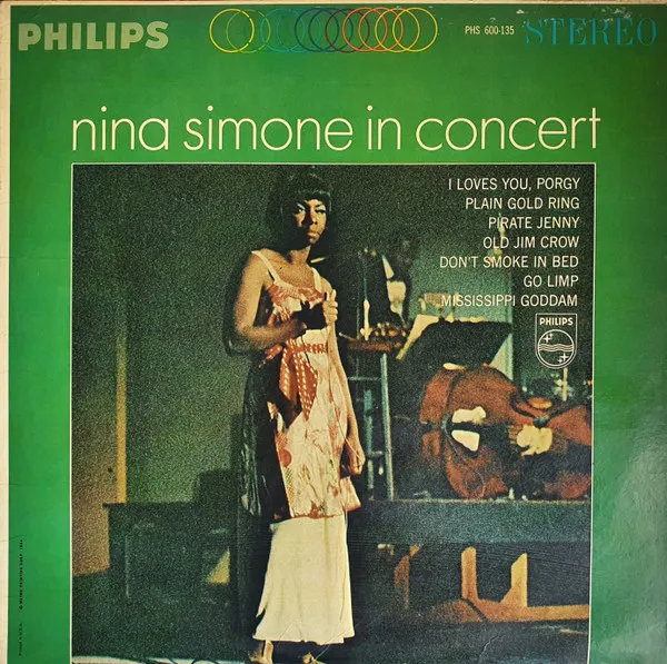 A green-bordered LP sleeve featuring a grainy stage photograph of a woman in a long pale patterned gown standing beside instruments in dim light, with a track list in cream type to the right.