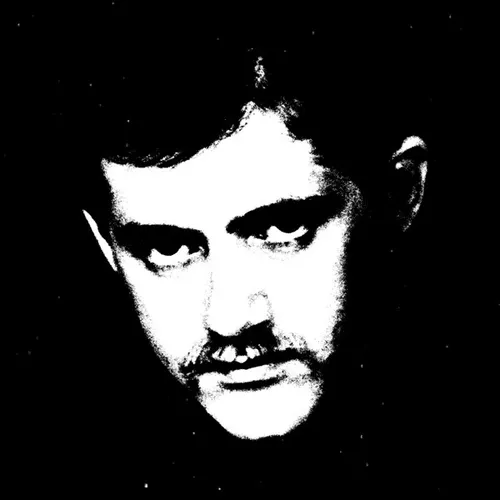 High-contrast black-and-white image of a mustachioed man's face staring intently at the viewer, his features reduced to stark white shapes emerging from a solid black background flecked with small white specks.