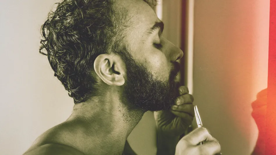 My partner, Sir Aditya, a lean and handsome brown-skinned Man with a a dark black and dense cropped beard stands shirtless in front of a mirror while primping and prepares to go out for the night by trimming His beard’s hairs with a pair of scissors.