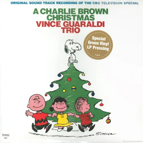 Three cartoon children hold hands dancing around a decorated green Christmas tree topped by a white beagle standing on its peak, with a yellow star ornament and colorful baubles, all set against a plain white background beneath green and red text.